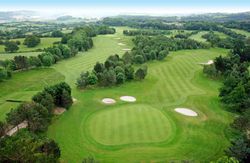 Aerial view of a lush green golf course with fairways, greens, sand bunkers, and surrounding trees.