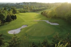 Aerial view of a golf course showing a green surrounded by sand bunkers and lush trees.