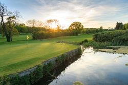 Golf course green next to a pond during sunset