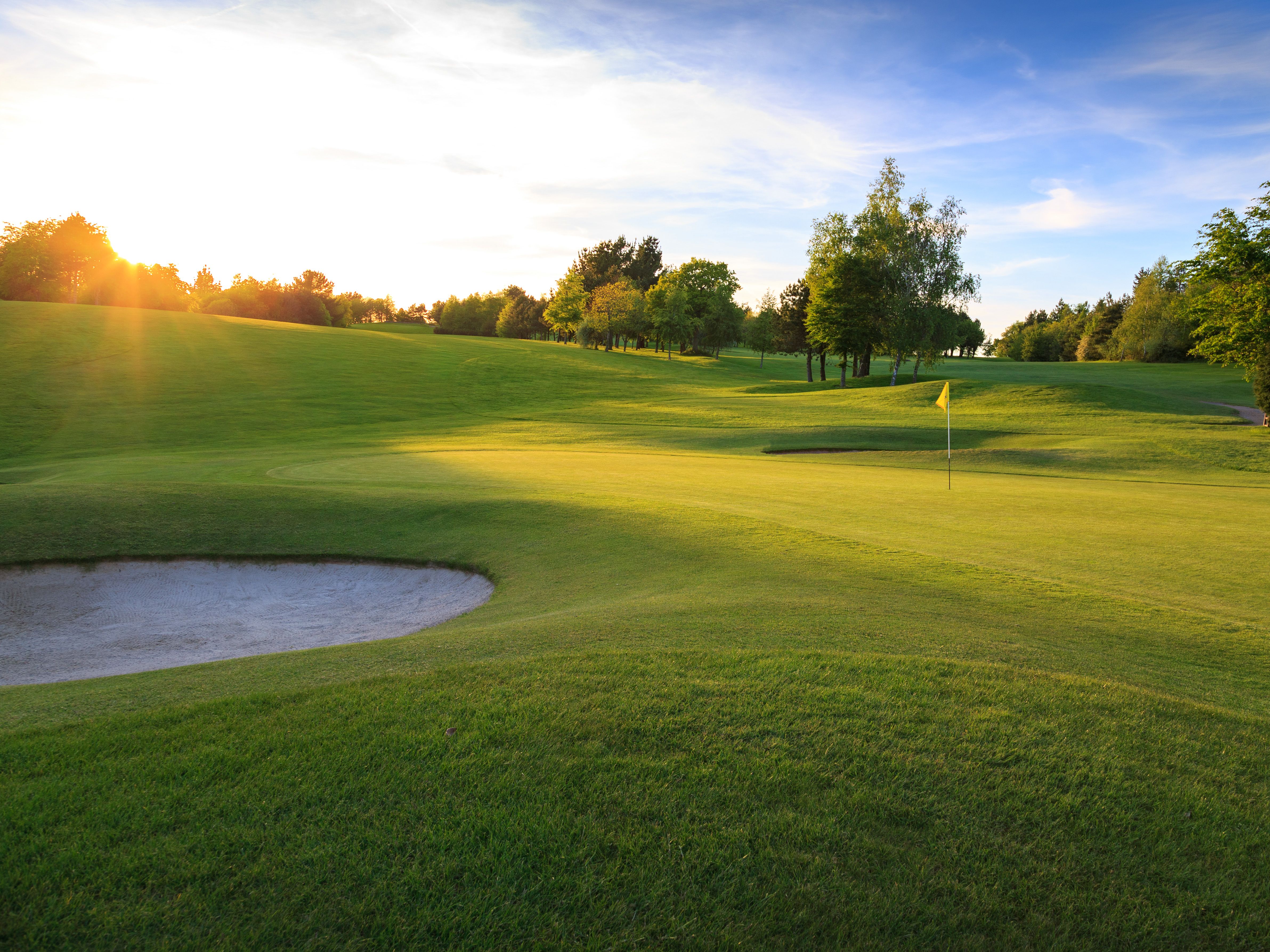 Golf course with a sand bunker and flagstick at sunset