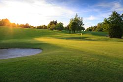 Golf course with a sand bunker and flagstick at sunset