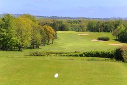 Scenic view of a golf course with sand bunkers and trees under a blue sky.