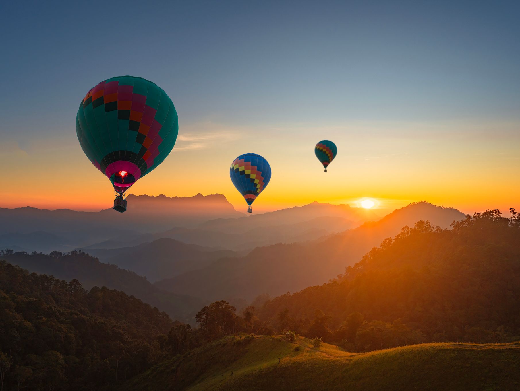 3 Hot air balloons over hills with a orange sunset background