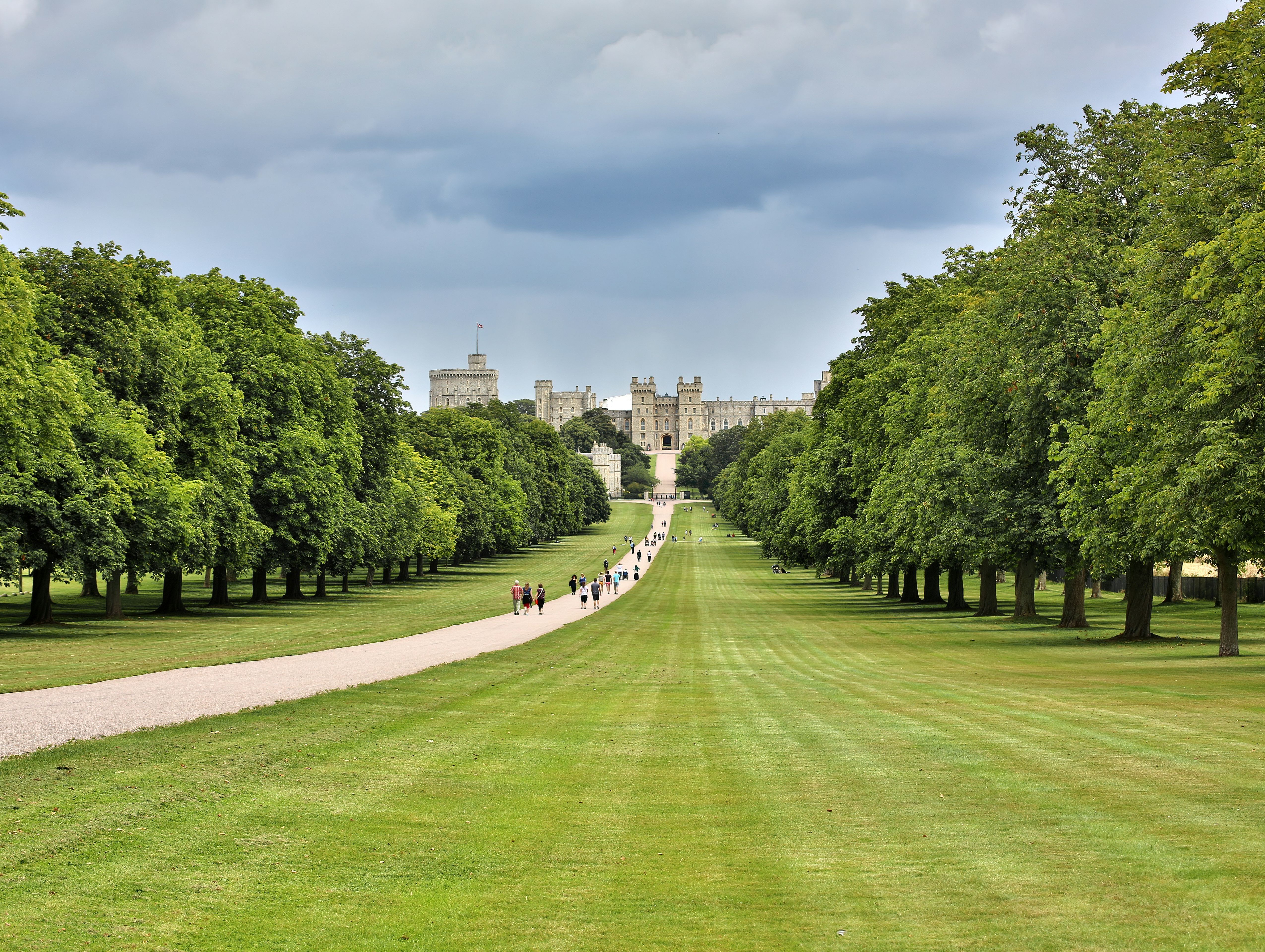 A long gravel path leads up to Window Castel in the distance, with mowed green grass in the foreground and the path is framed by green leafy trees.