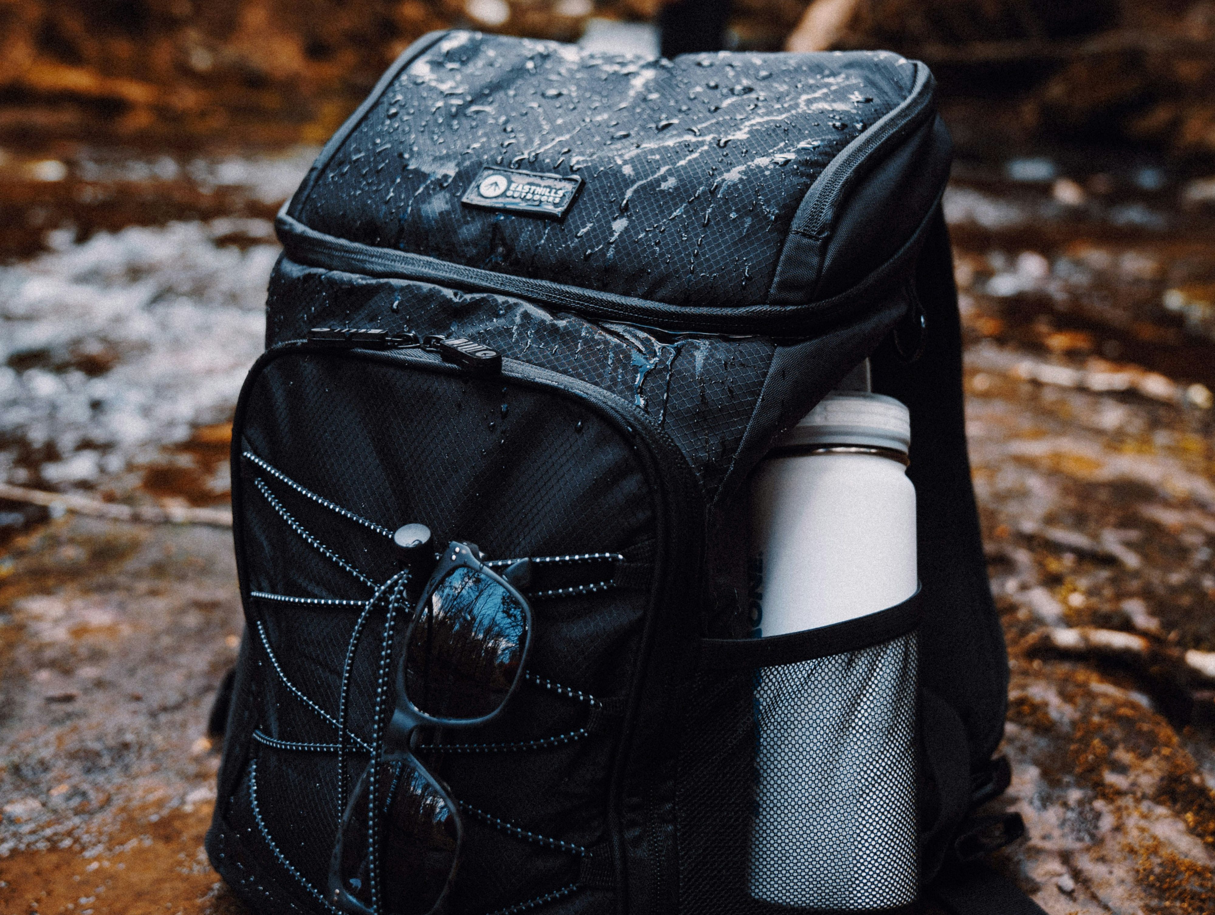 A black rucksack is in the foreground with a white water bottle.