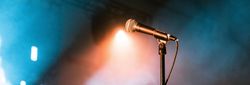 Microphone on stand under stage lights with atmospheric blue and orange smoke in the background.