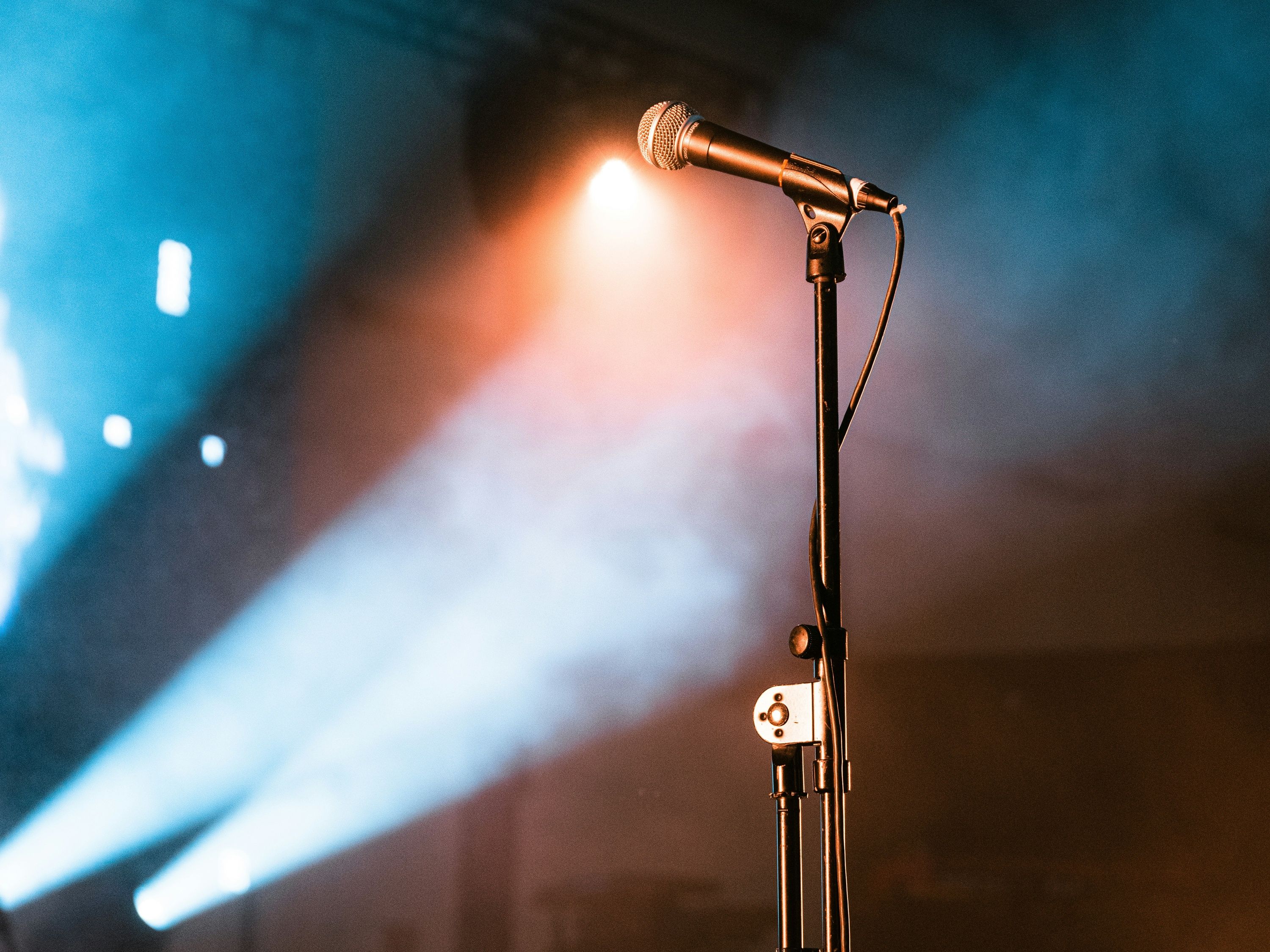Microphone on stand under stage lights with atmospheric blue and orange smoke in the background.