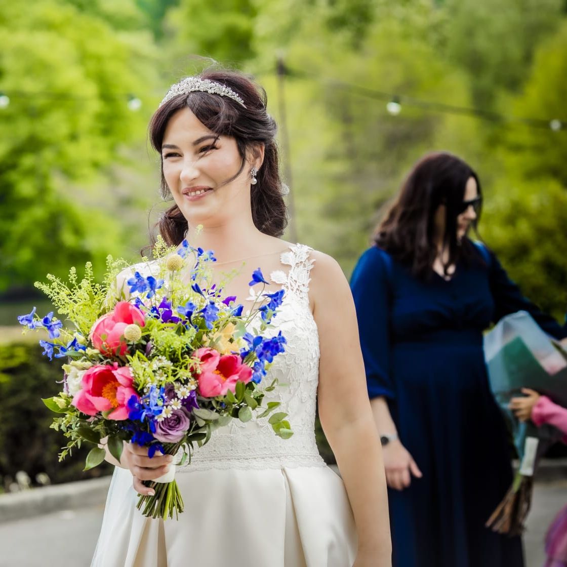 A bride is smiling with a colourful bouquet of flowers in her hand