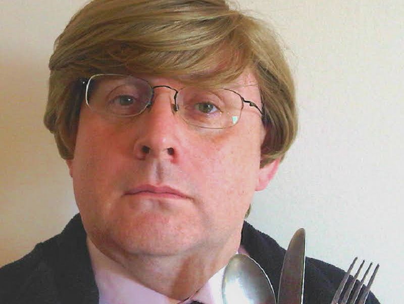 Person with glasses holding a spoon, knife, and fork