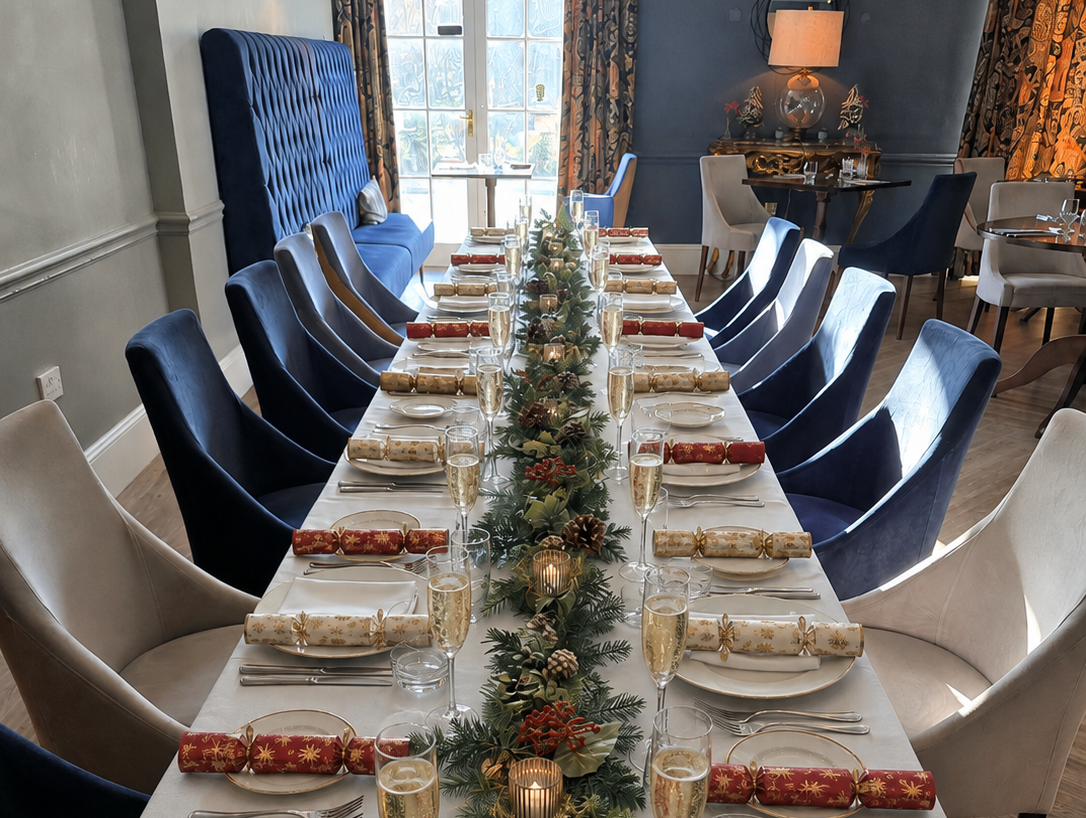 Long restaurant table set for Christmas dinner with crackers, candles and festive greenery centrepiece