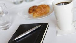 Notepad on a white table cloth with a cup of coffee and pastries