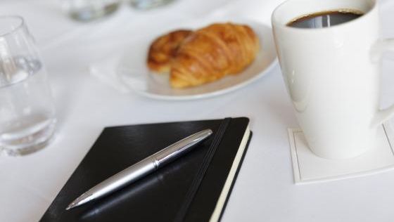 Notepad on a white table cloth with a cup of coffee and pastries