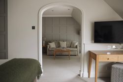 Modern neutral toned hotel room with a seating area visible through an archway, a desk, and a wall-mounted TV.