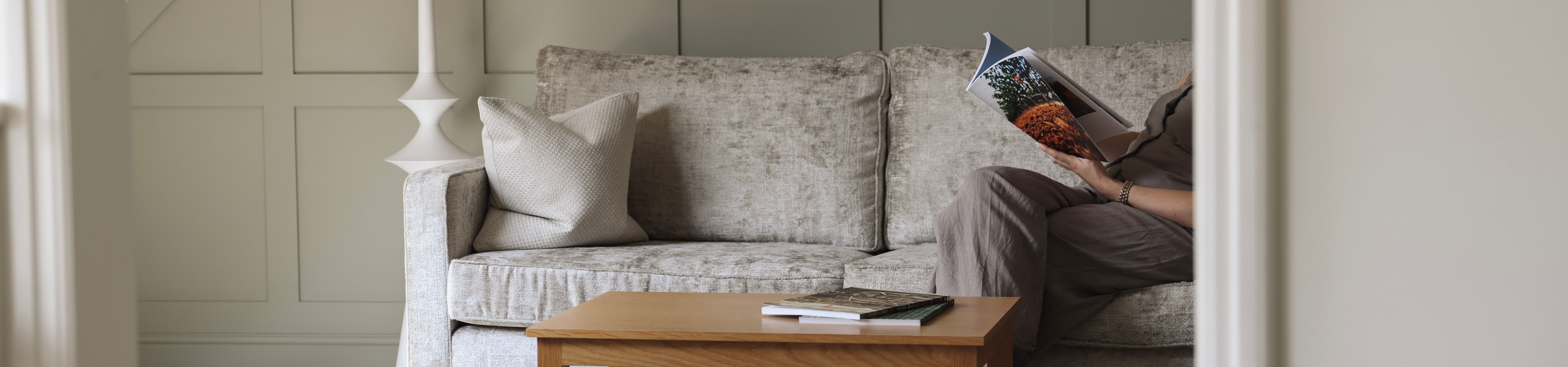 A cozy living area with a light grey sofa, wooden coffee table, and a person reading a magazine.