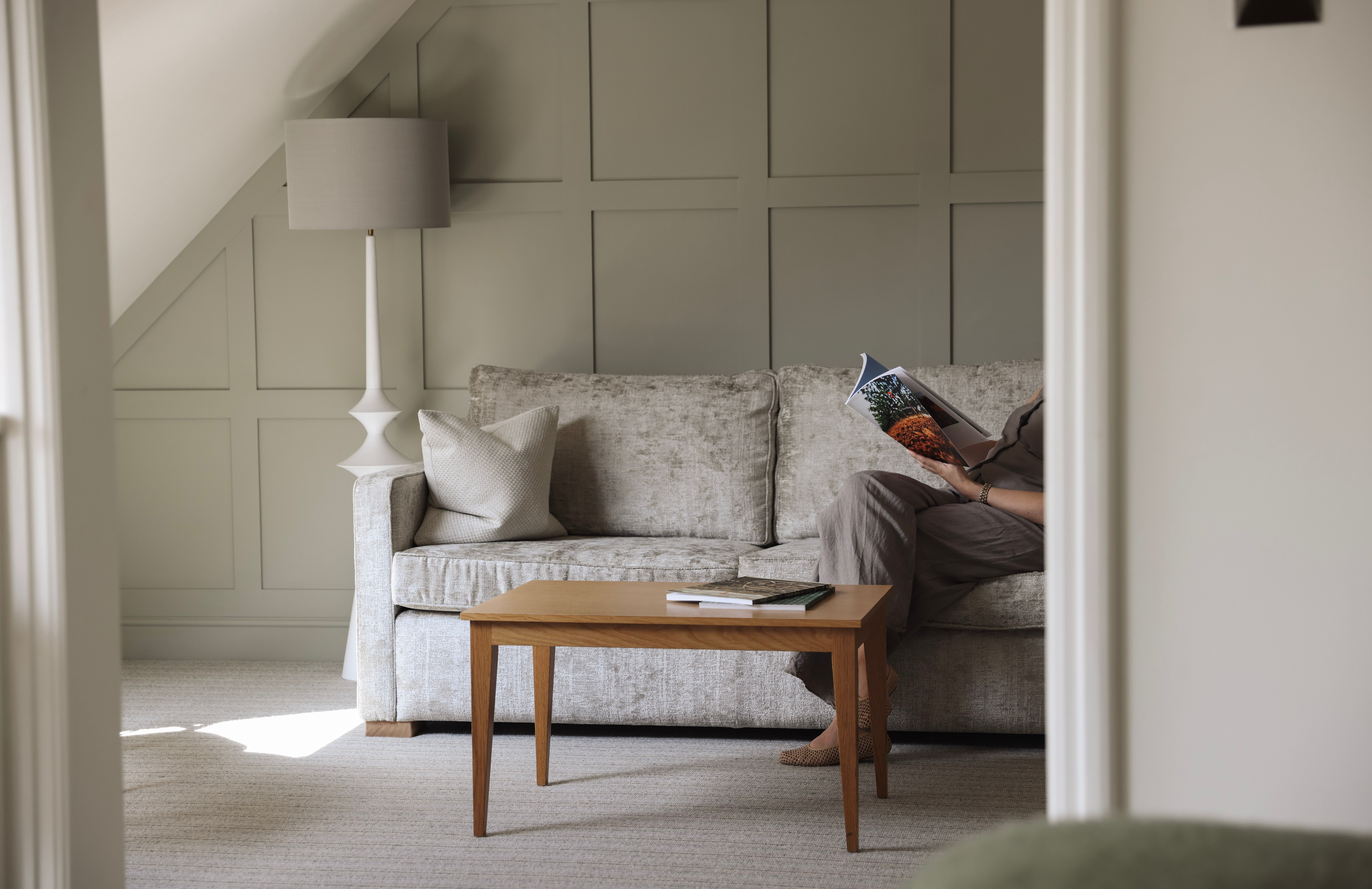 A cozy living area with a light grey sofa, wooden coffee table, and a person reading a magazine.
