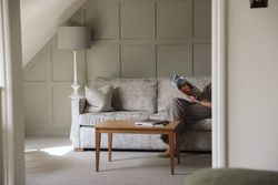 A cozy living area with a light grey sofa, wooden coffee table, and a person reading a magazine.