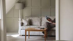 A cozy living area with a light grey sofa, wooden coffee table, and a person reading a magazine.