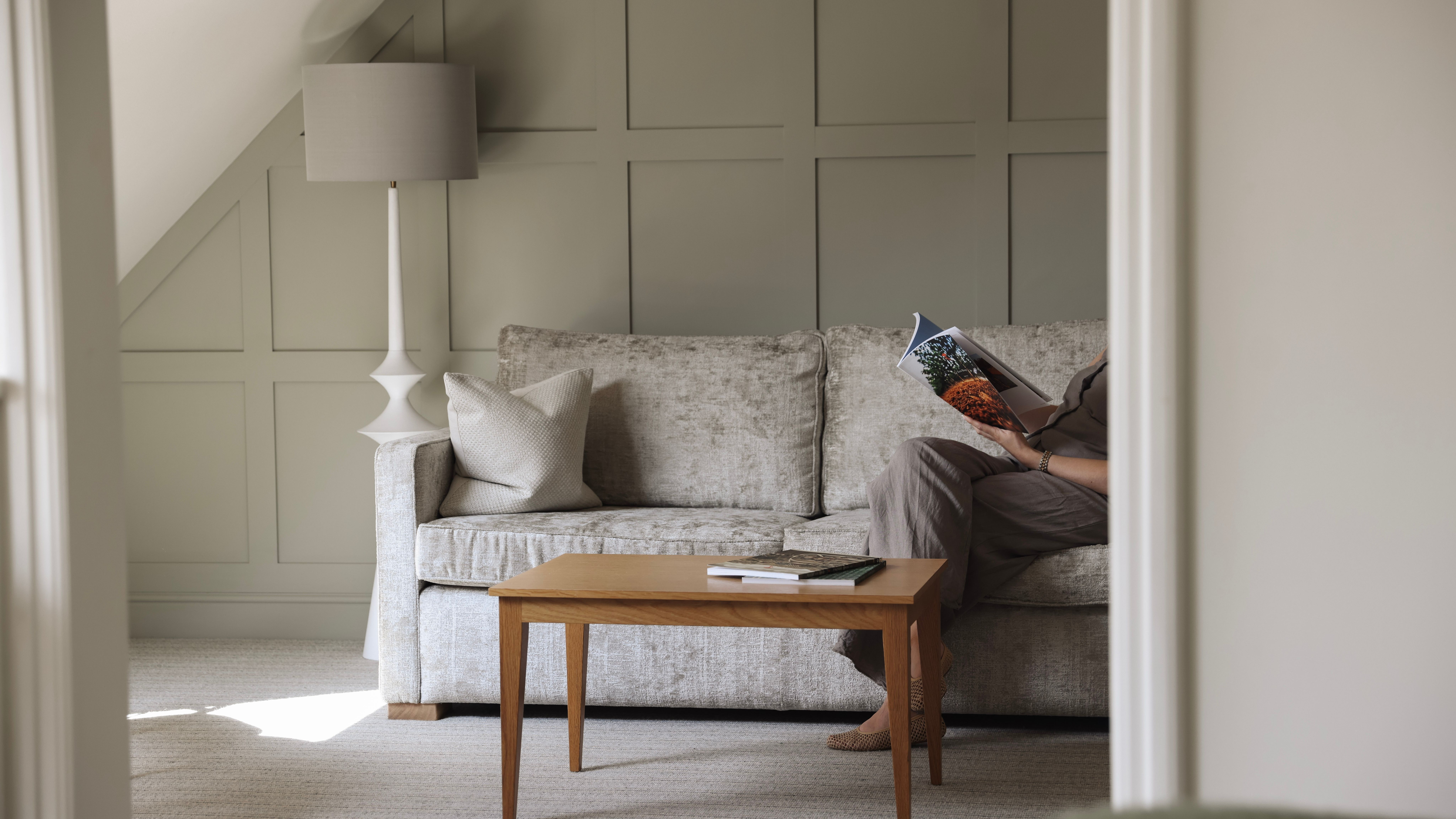 A cozy living area with a light grey sofa, wooden coffee table, and a person reading a magazine.