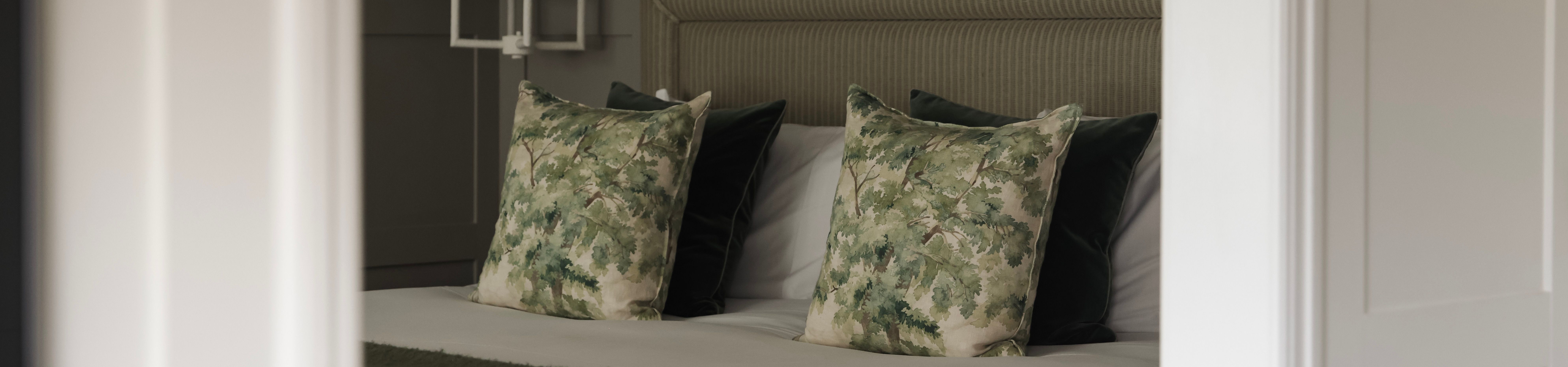 A modern bed with green-themed decor and leafy patterned pillows in a cozy bedroom.