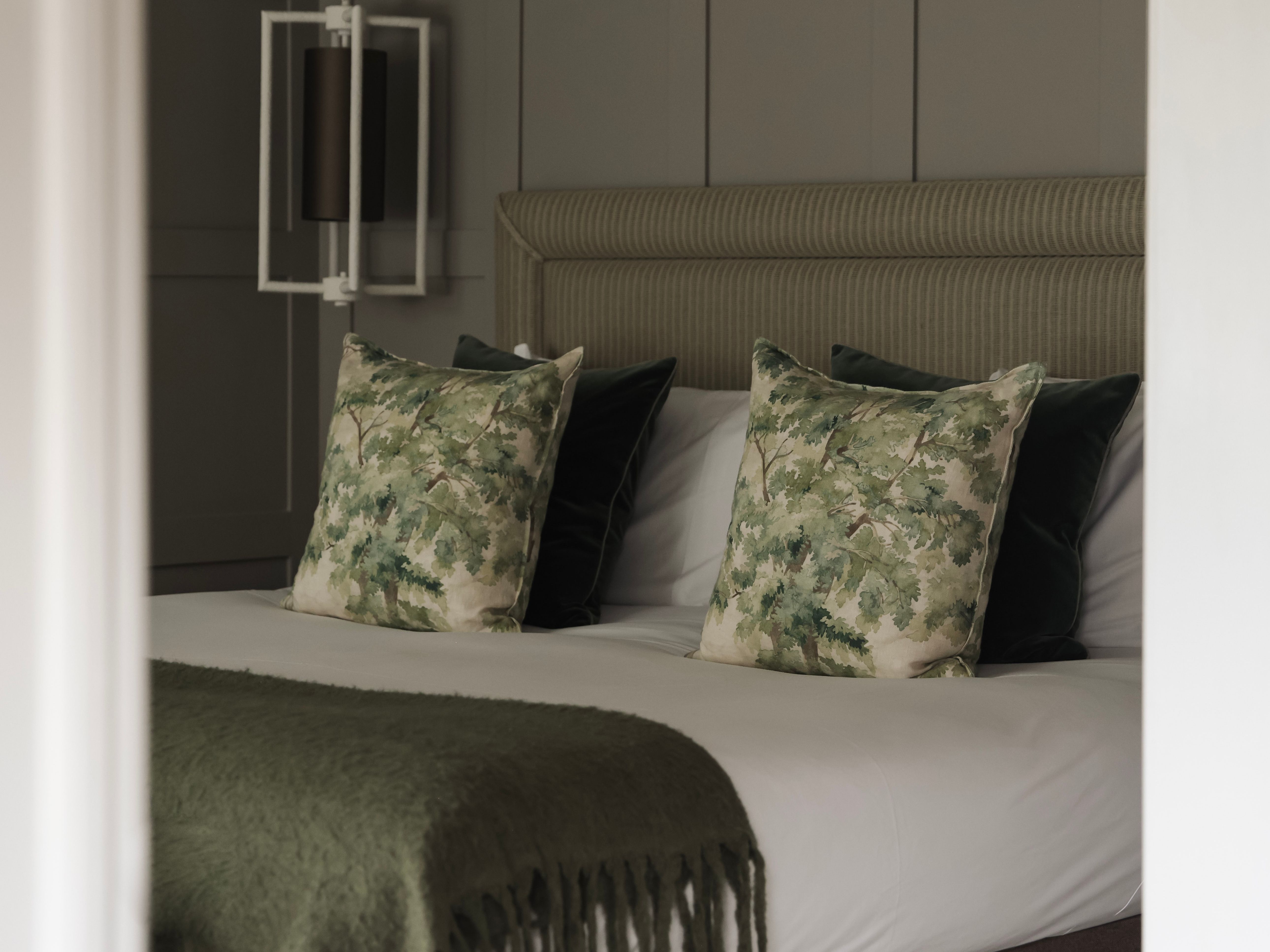 A modern bed with green-themed decor and leafy patterned pillows in a cozy bedroom.