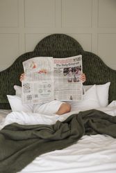 Person sitting in bed reading The Daily Telegraph newspaper, partially covered by a green blanket.