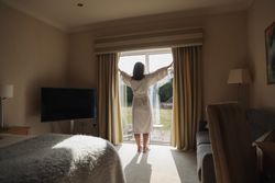 Woman in a bathrobe opening curtains in a cozy bedroom with a view of the garden