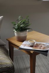Wooden side table with a potted fern, a cup of coffee, and a magazine