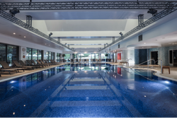 Indoor swimming pool with lounge chairs along the sides and large windows