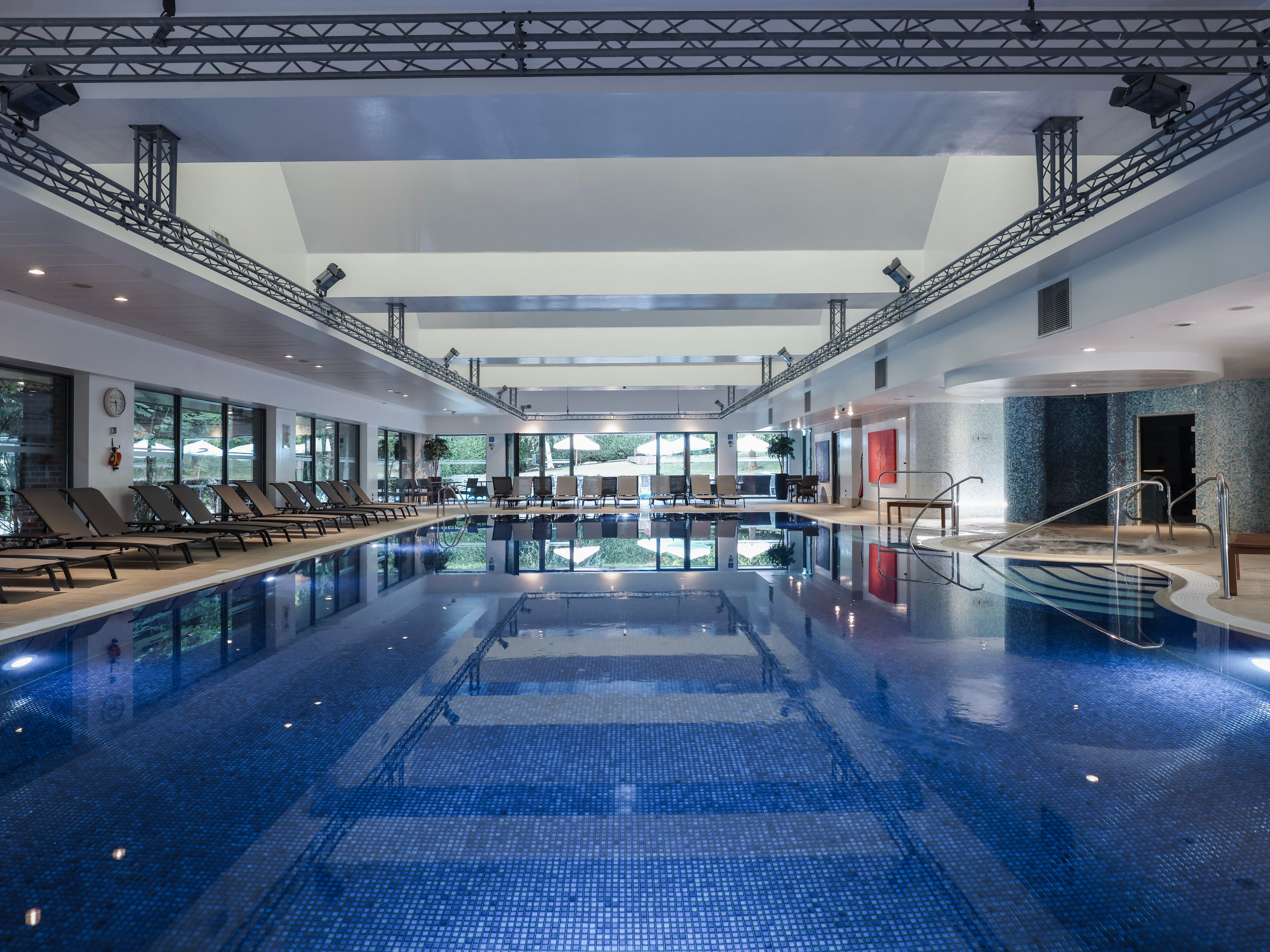 Indoor swimming pool with lounge chairs along the sides and large windows