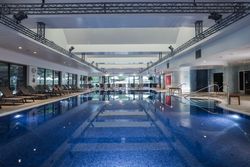 Indoor swimming pool with lounge chairs along the sides and large windows