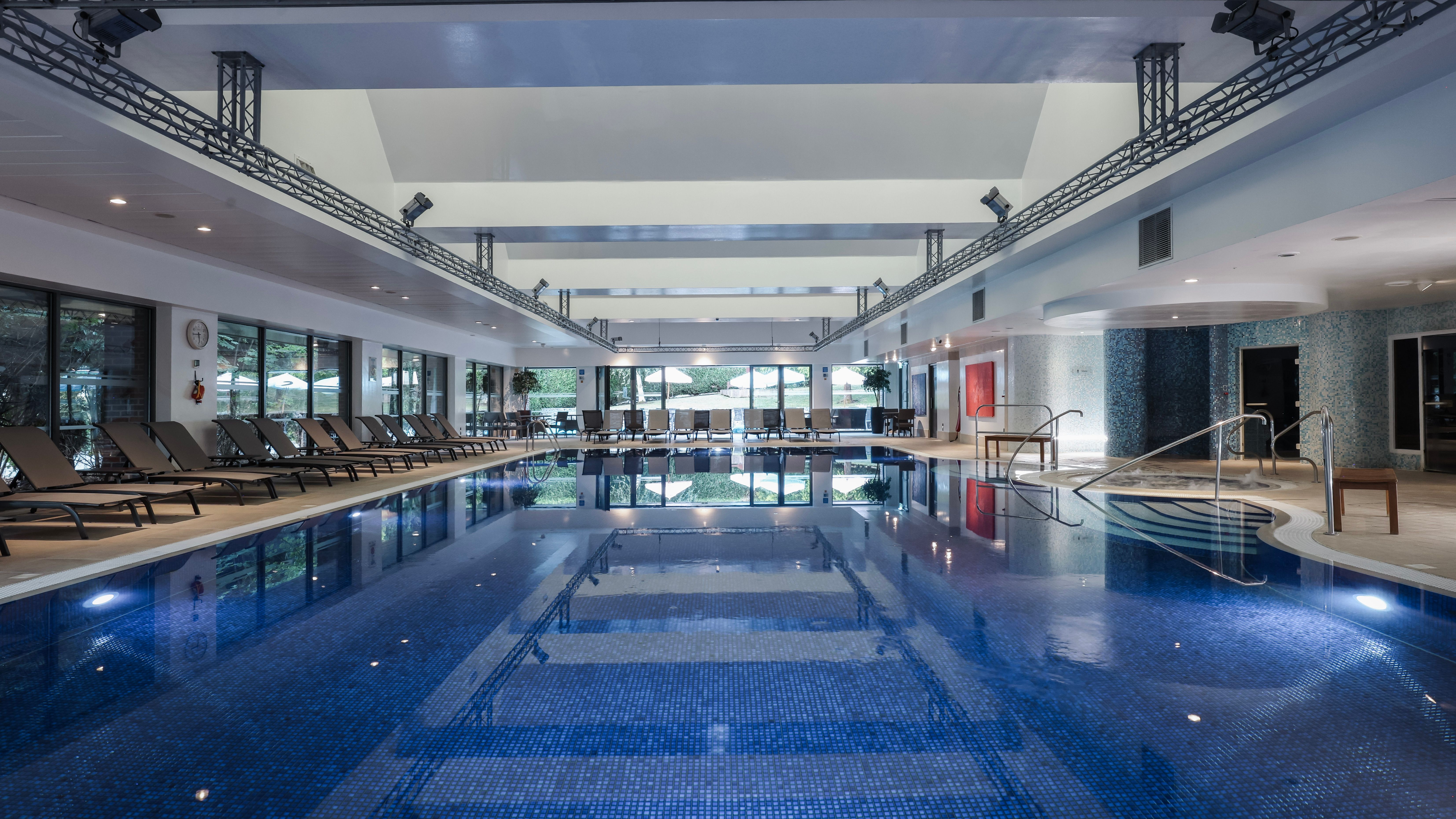 Indoor swimming pool with lounge chairs along the sides and large windows
