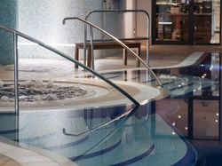 Indoor swimming pool with steps, handrails, and a bubbling spa section