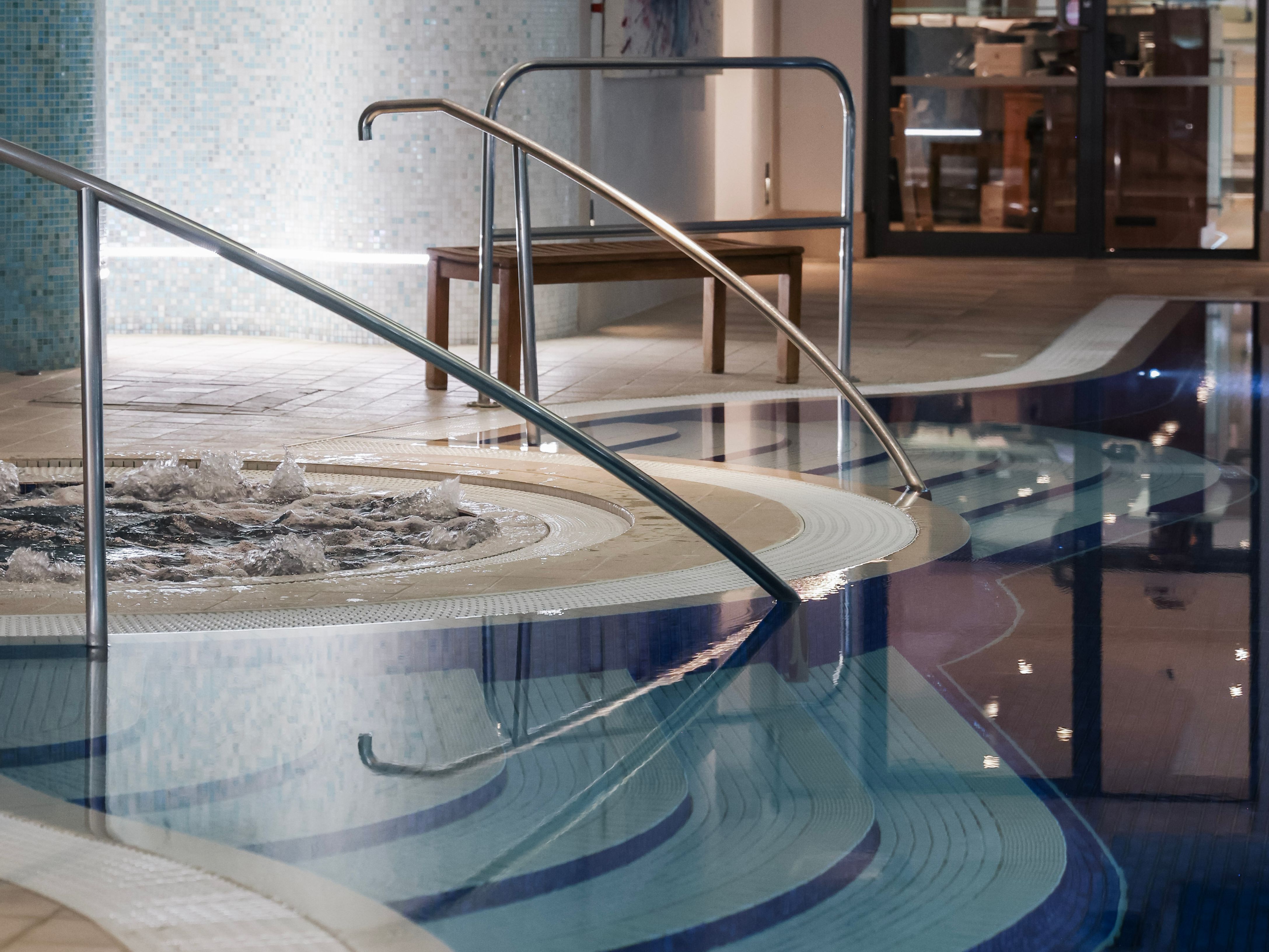 Indoor swimming pool with steps, handrails, and a bubbling spa section