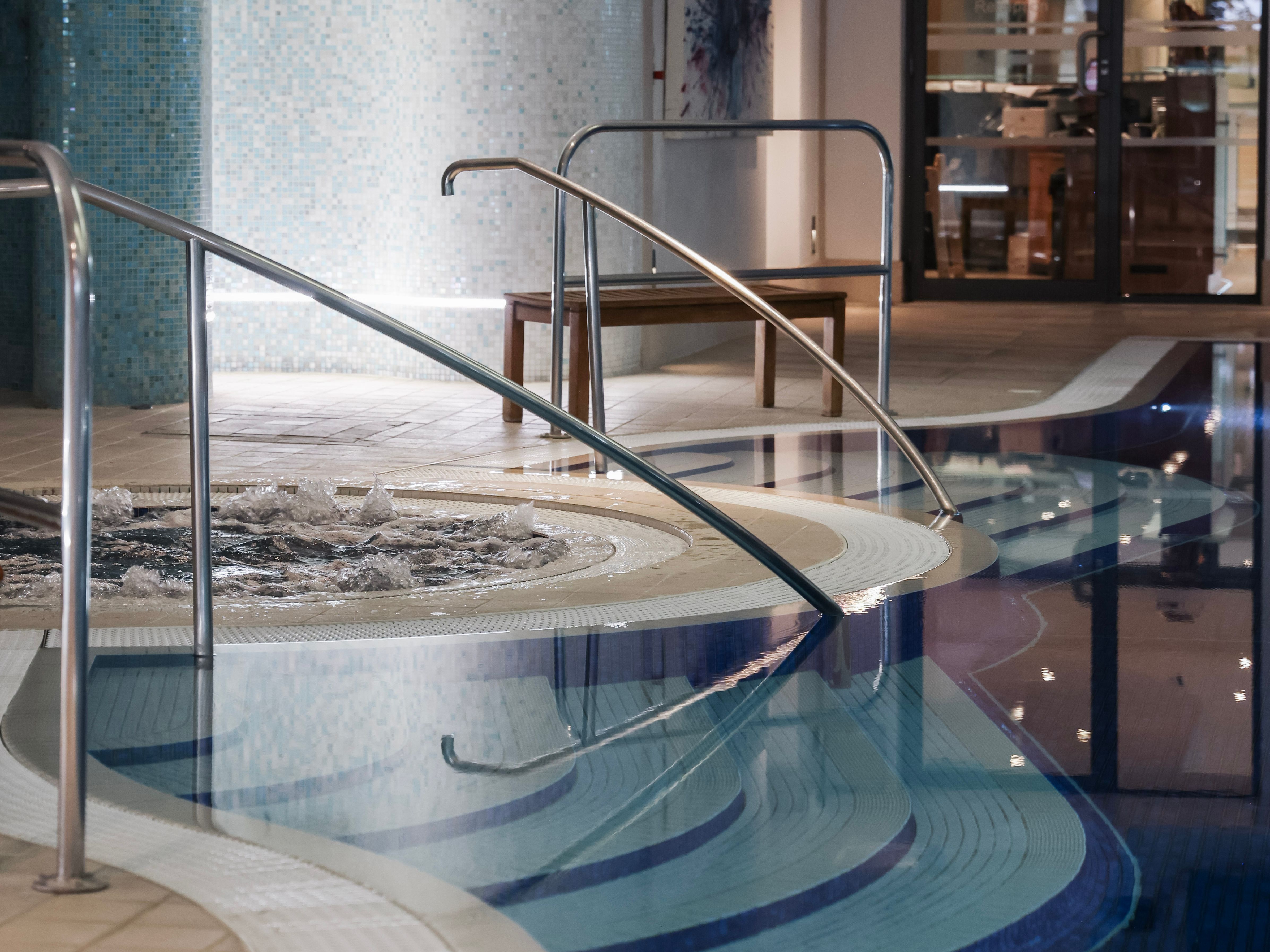 Indoor swimming pool with steps, handrails, and a bubbling spa section