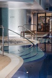Indoor swimming pool with steps, handrails, and a bubbling spa section