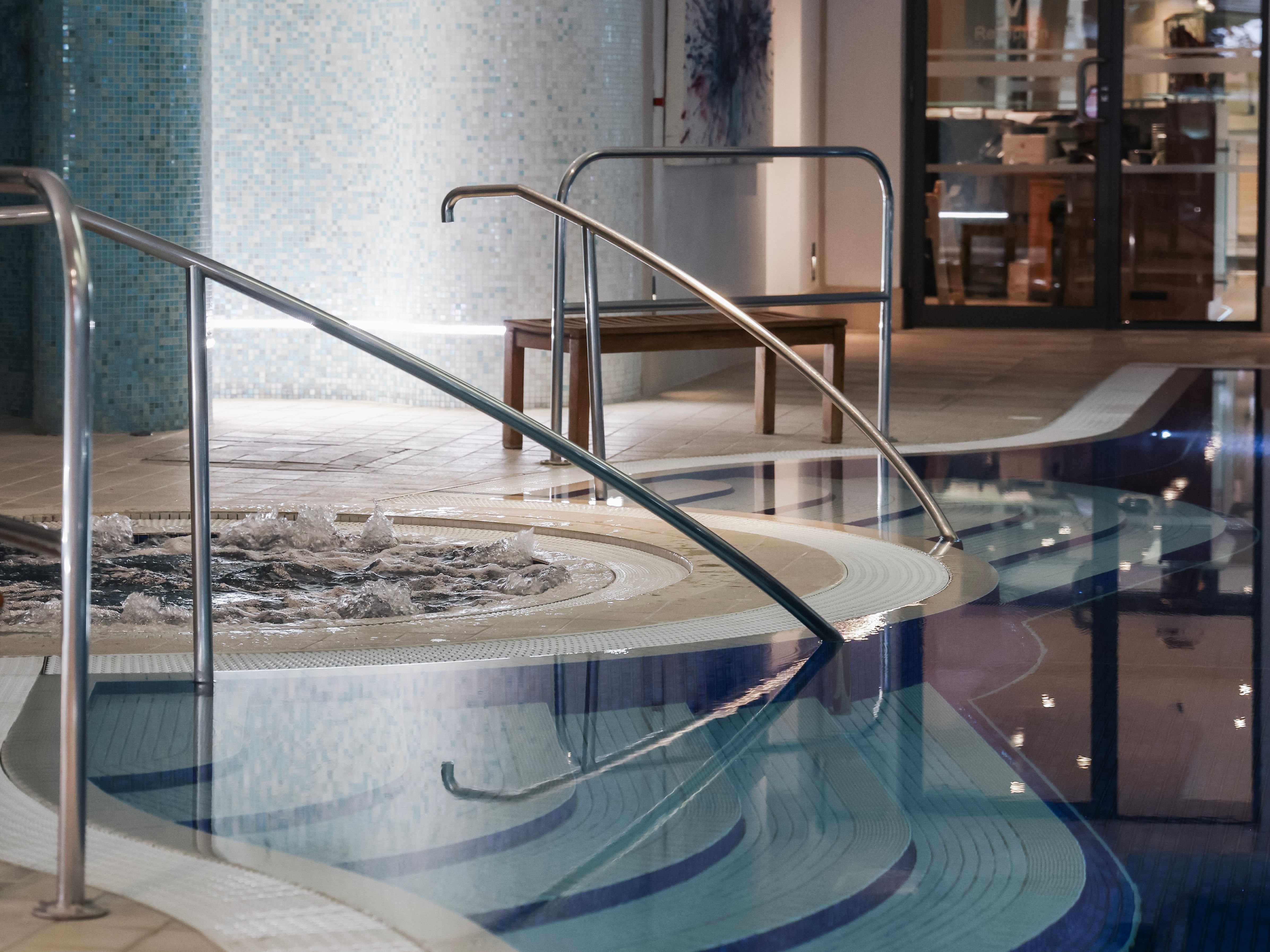 Indoor swimming pool with steps, handrails, and a bubbling spa section