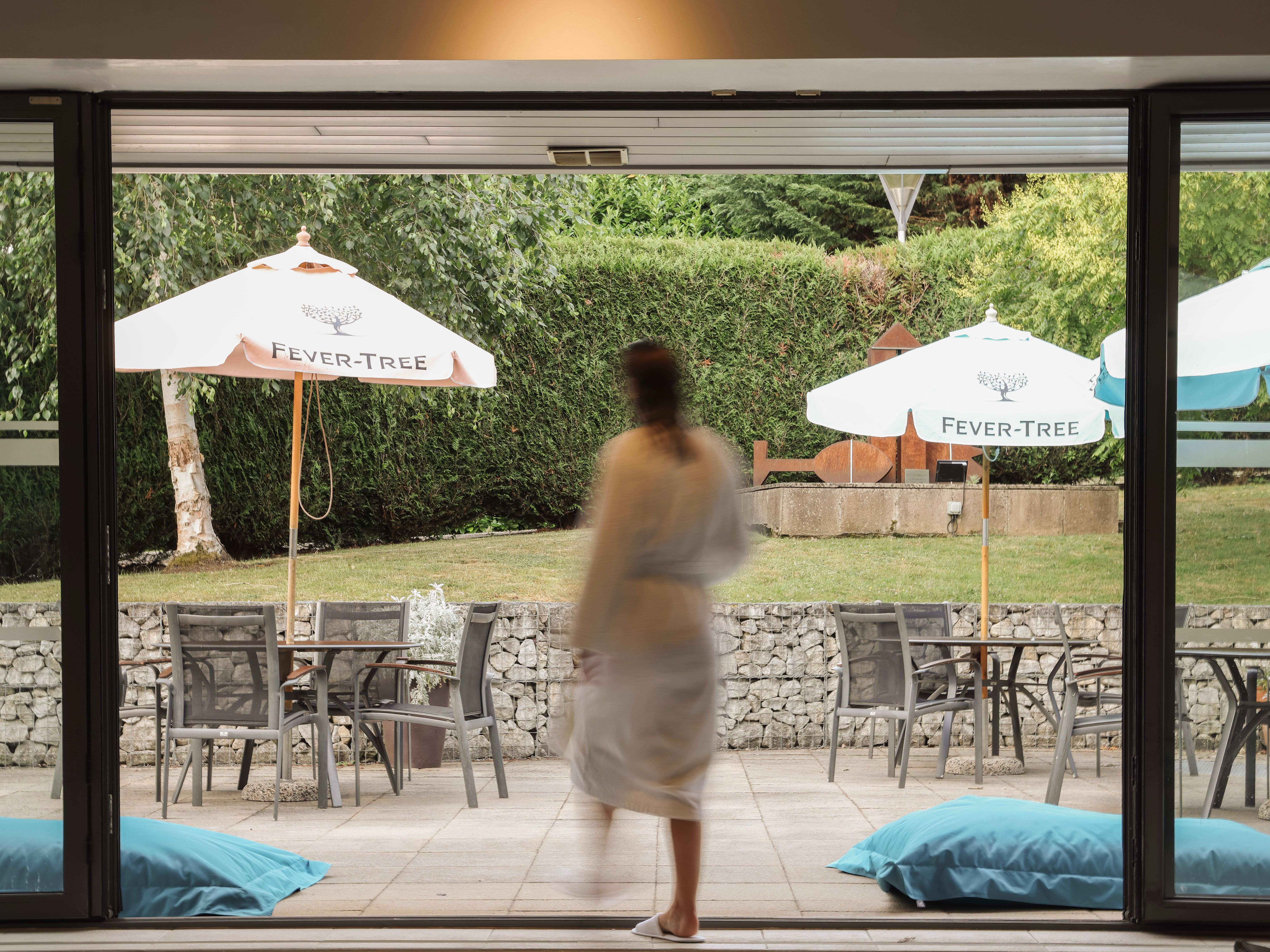 Person in a robe walking towards an outdoor seating area with white Fever-Tree umbrellas.