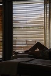 Person lounging on a chair in front of a window with closed blinds.