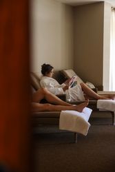 Woman in a white robe relaxing on a lounge chair while reading a magazine in a spa setting.