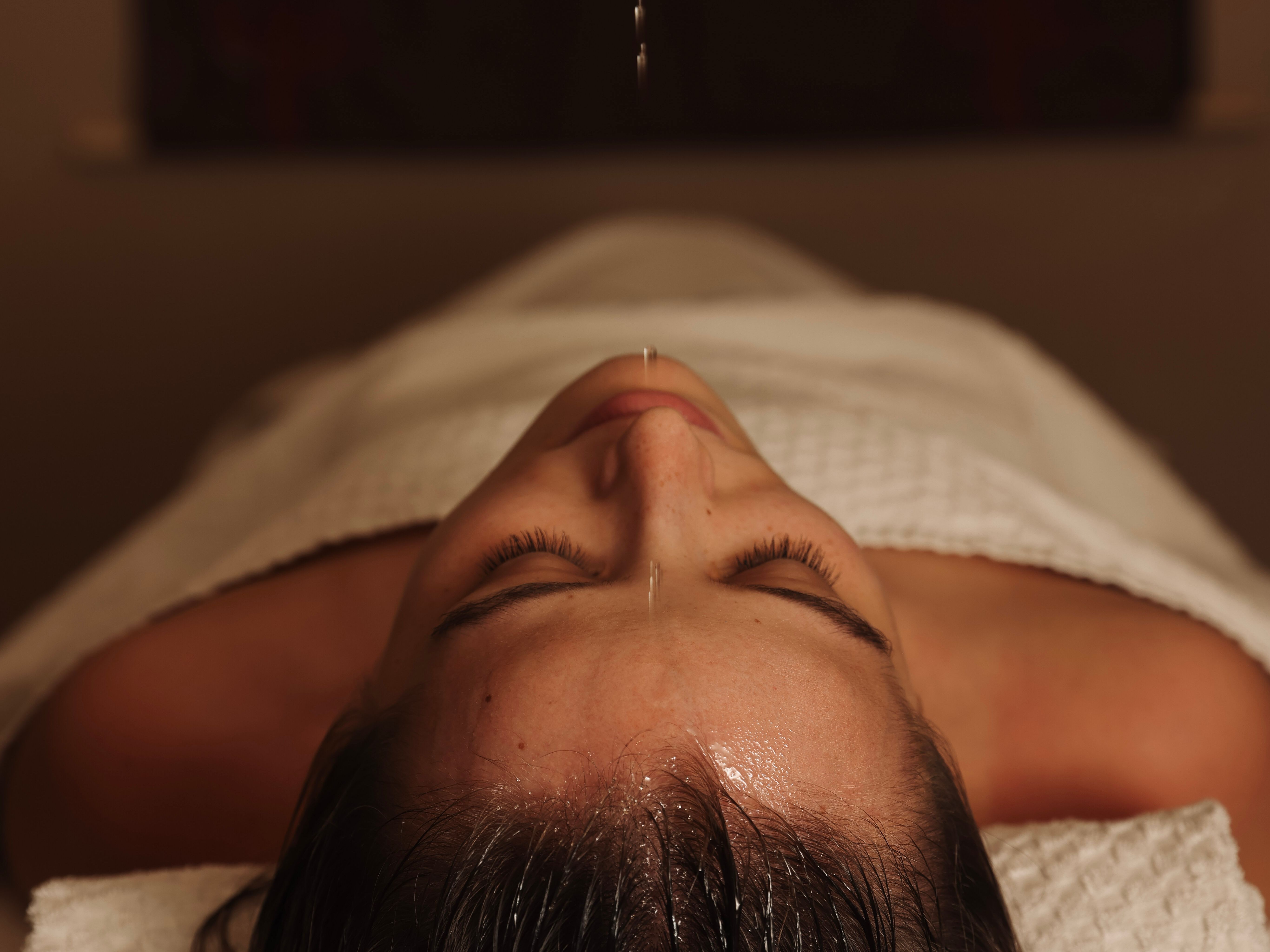 Person lying down with oil dripping onto their forehead during a spa treatment