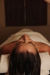 Person lying down with oil dripping onto their forehead during a spa treatment