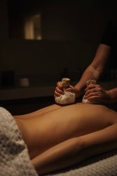 A person receiving a herbal compress massage in a dimly lit spa room.