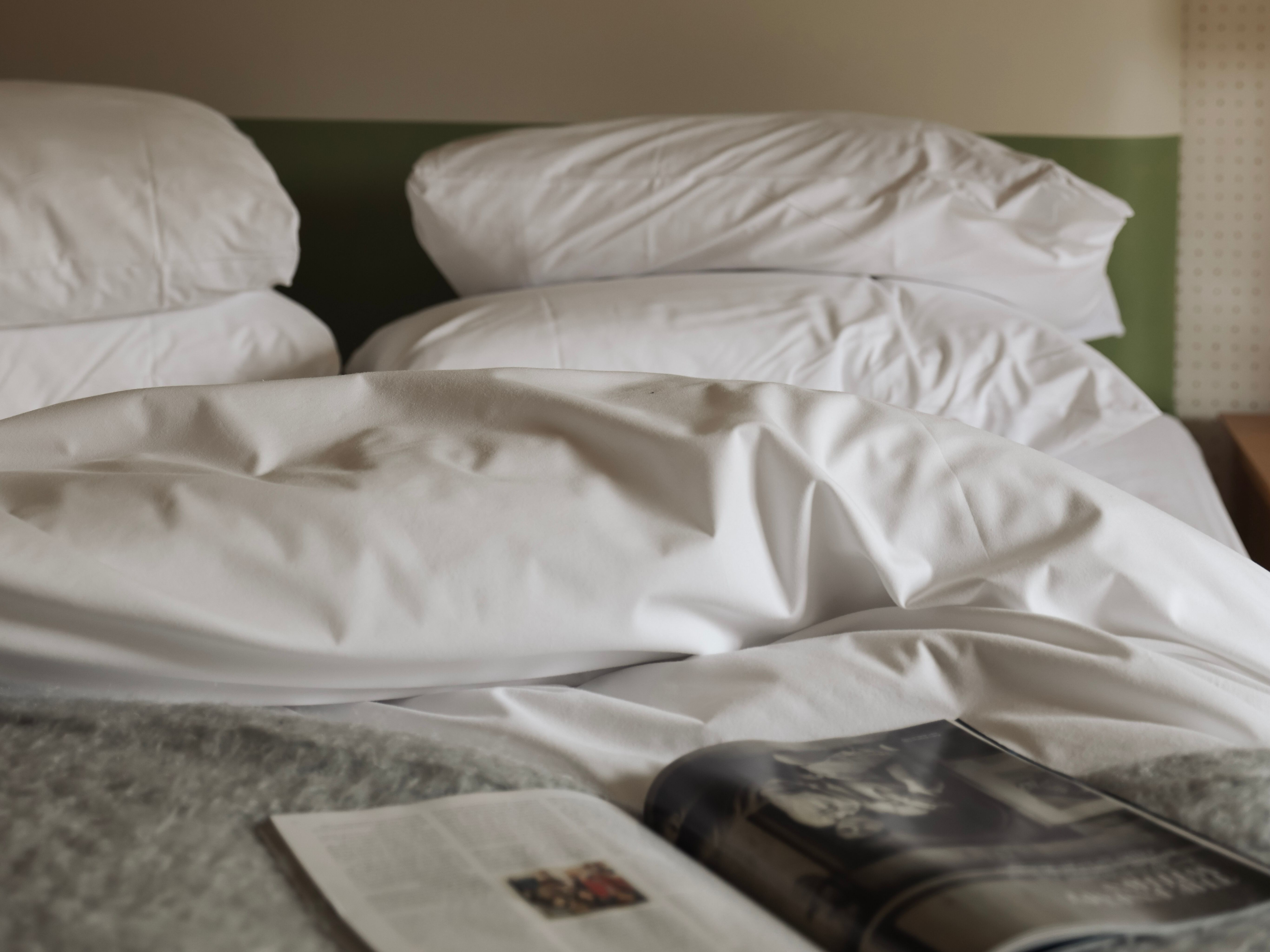 Unmade bed with white pillows and sheets, a magazine lying open on the bed