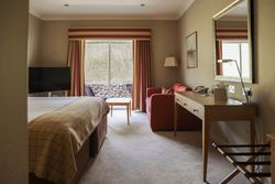 A cozy hotel room with a large bed, red sofa, desk with mirror, and sliding glass doors leading outside.