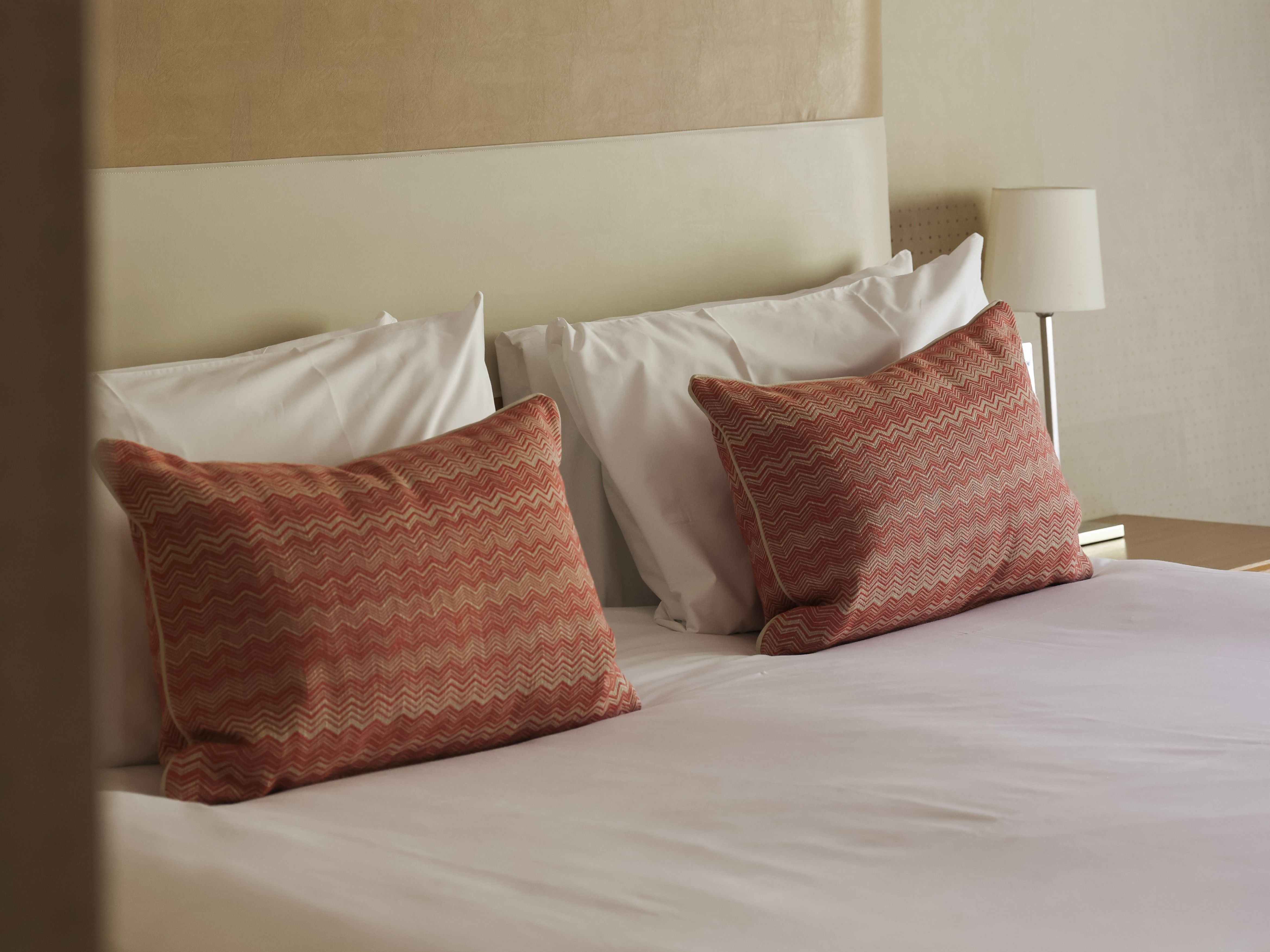 Modern hotel bed with two decorative red pillows and white linens