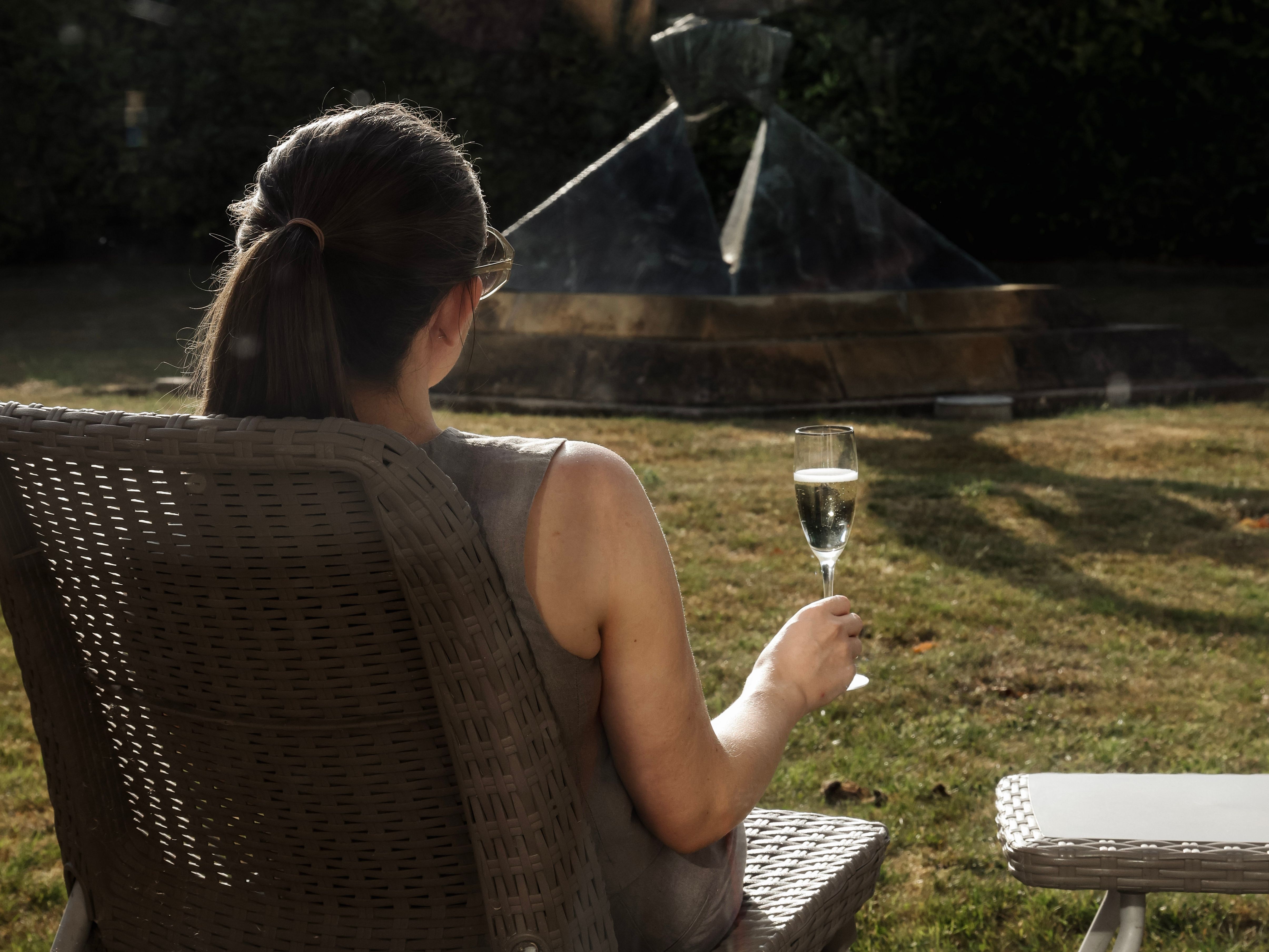Woman sitting outdoors in a wicker chair holding a glass of champagne, facing a modern garden sculpture