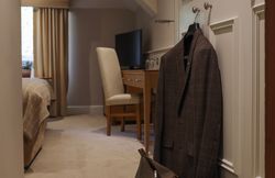 A cozy hotel room with a suit hanging on the door and a travel bag on the floor.