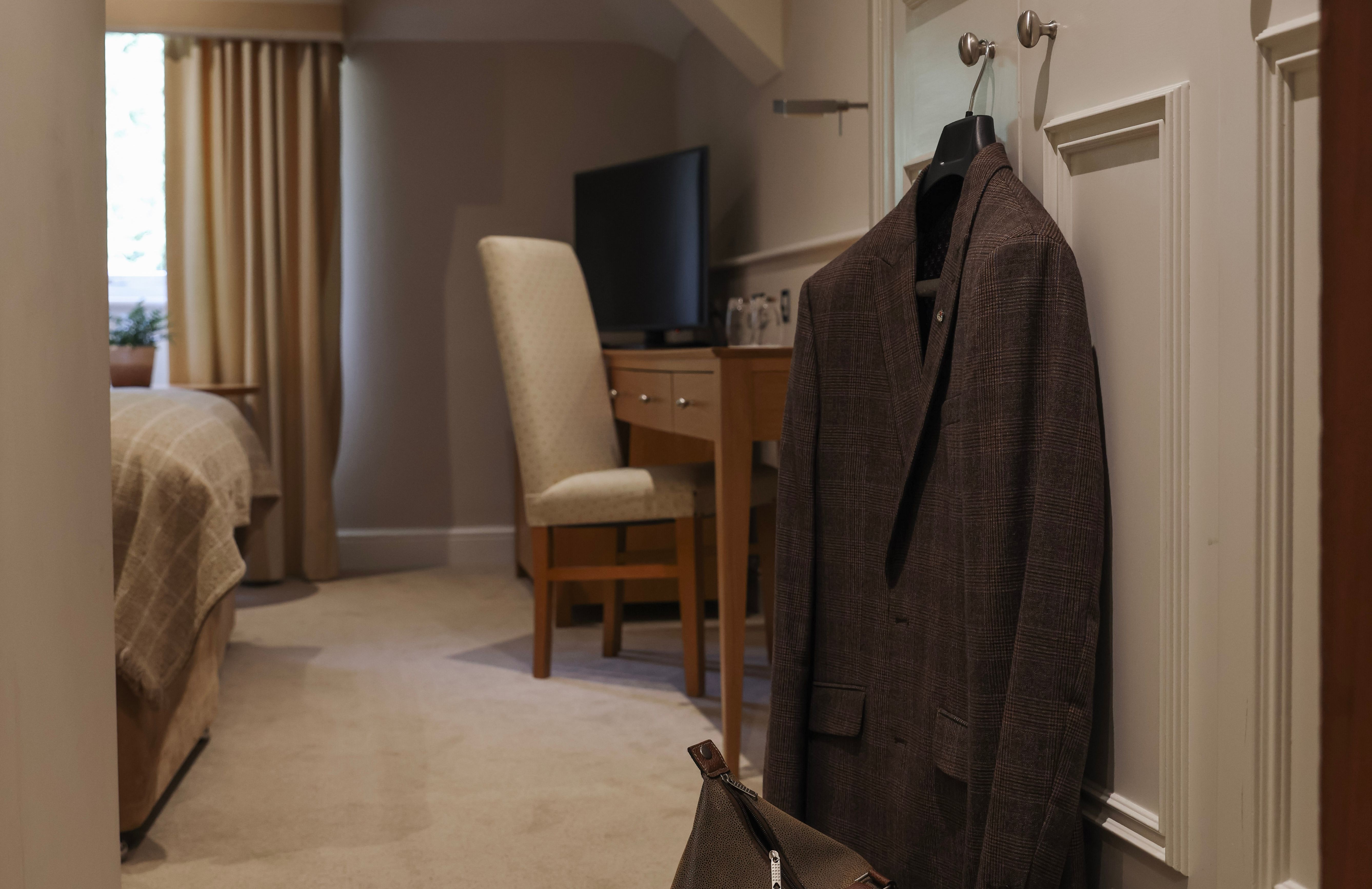 A cozy hotel room with a suit hanging on the door and a travel bag on the floor.