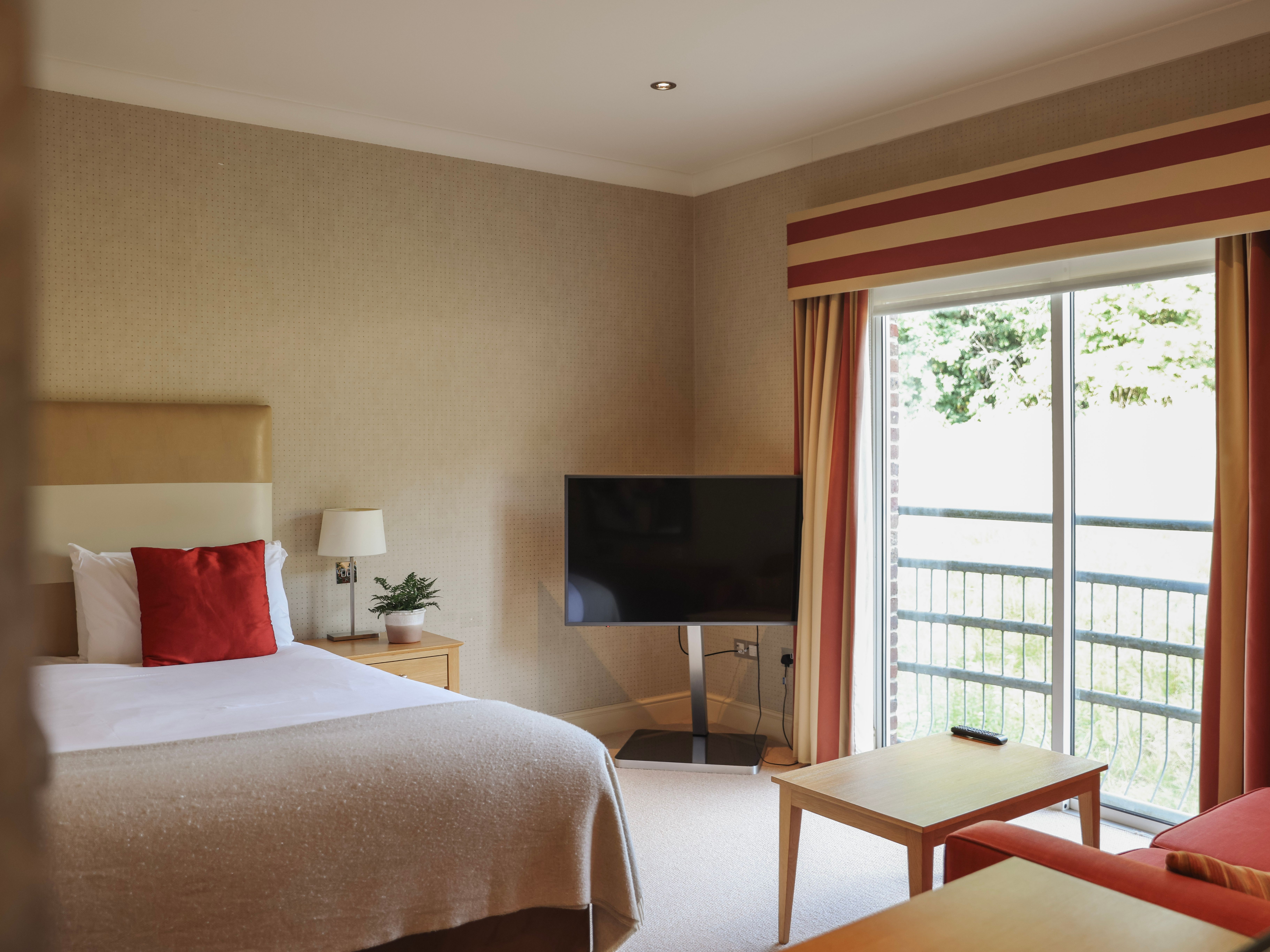 Modern hotel room with a bed, television, window with curtains, and a balcony view