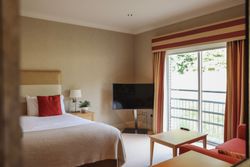 Modern hotel room with a bed, television, window with curtains, and a balcony view